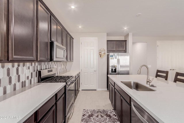 kitchen featuring dark brown cabinetry, sink, backsplash, a kitchen bar, and appliances with stainless steel finishes