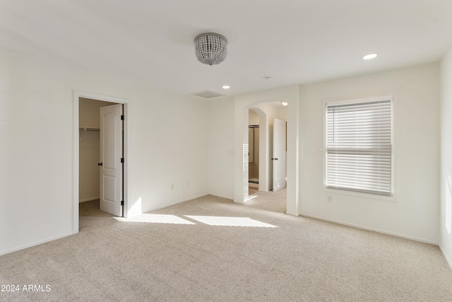 unfurnished bedroom with light colored carpet, a walk in closet, and a closet