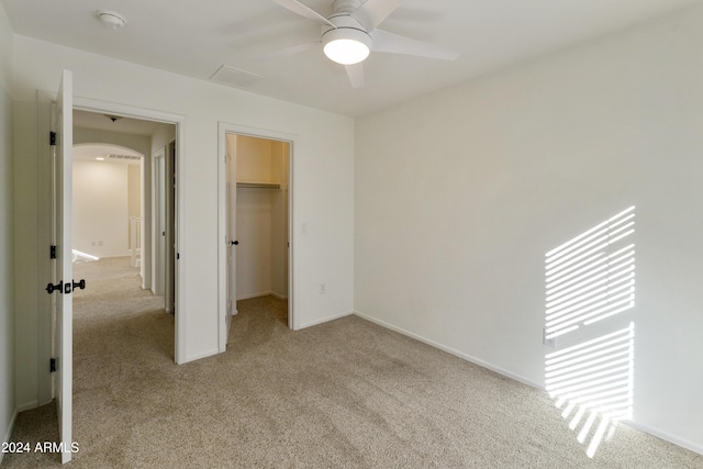 unfurnished bedroom with light carpet, a closet, a spacious closet, and ceiling fan