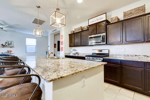 kitchen featuring dark brown cabinets, light stone countertops, decorative light fixtures, appliances with stainless steel finishes, and a sink