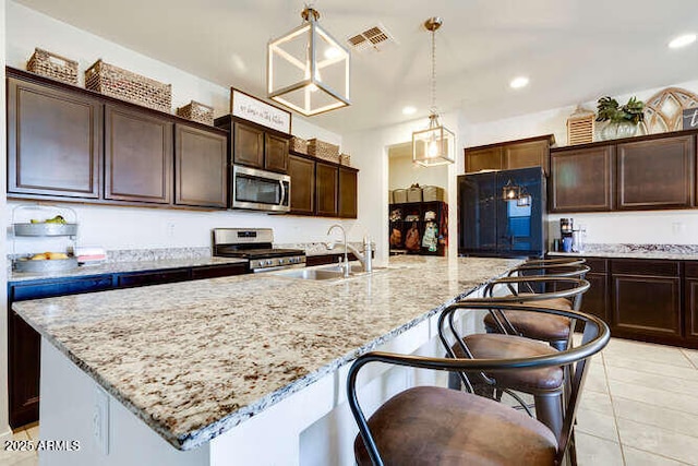 kitchen with dark brown cabinets, light stone counters, recessed lighting, stainless steel appliances, and a kitchen island with sink