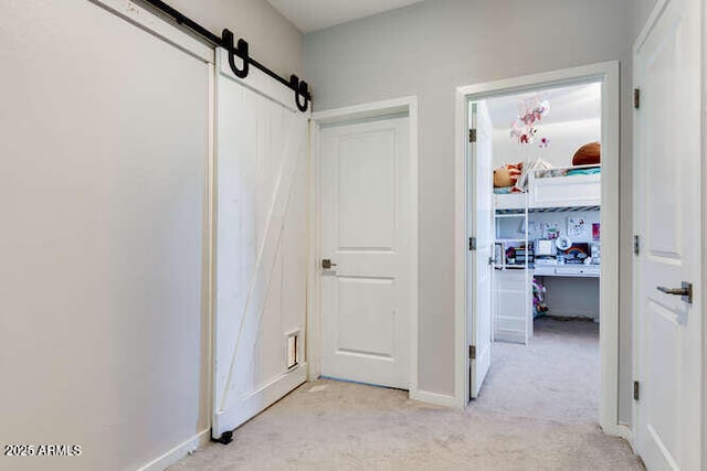 hall featuring a barn door, baseboards, and light carpet