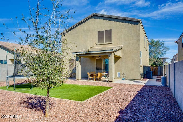 rear view of property featuring a patio, a fenced backyard, stucco siding, a trampoline, and a lawn