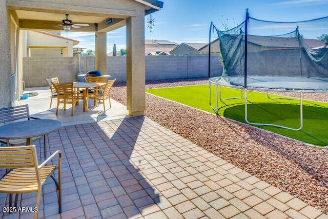 view of patio / terrace featuring a ceiling fan, outdoor dining area, a trampoline, and a fenced backyard