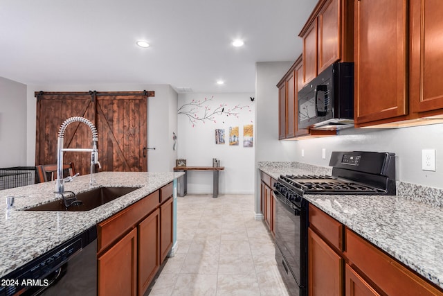 kitchen featuring light stone countertops, black appliances, sink, and a barn door