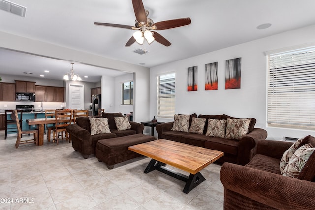 tiled living room with ceiling fan with notable chandelier