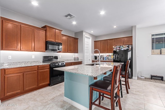 kitchen with light stone countertops, black appliances, sink, an island with sink, and a kitchen bar