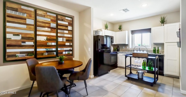 kitchen with black fridge, white cabinetry, and light tile patterned floors