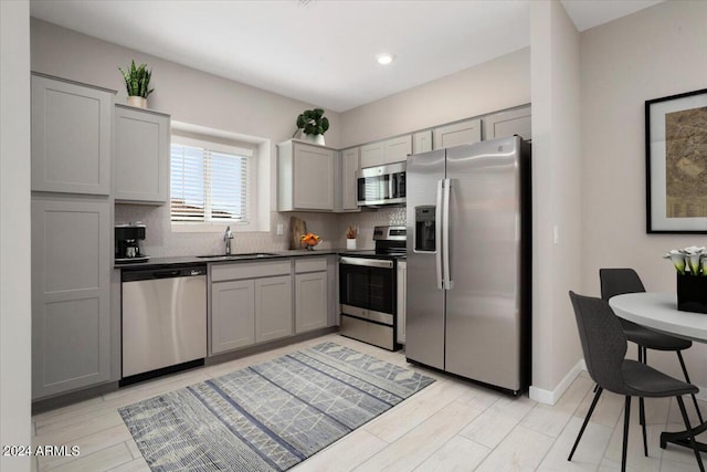 kitchen with gray cabinetry, backsplash, sink, light hardwood / wood-style floors, and stainless steel appliances