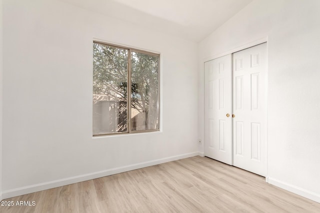 unfurnished bedroom with a closet, lofted ceiling, and light hardwood / wood-style flooring