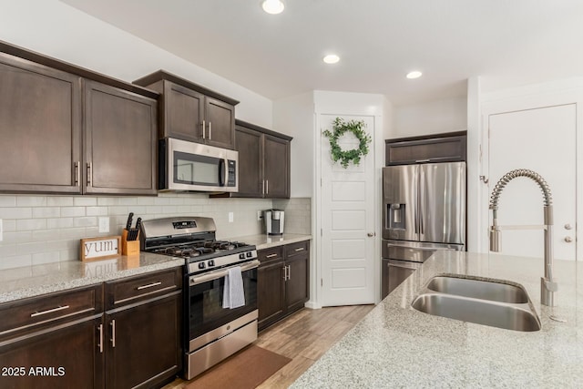 13380 N 148th Ave, Surprise, AZ 85379 - kitchen with stainless steel appliances, a sink, dark brown cabinetry, light stone countertops, and light wood finished floors