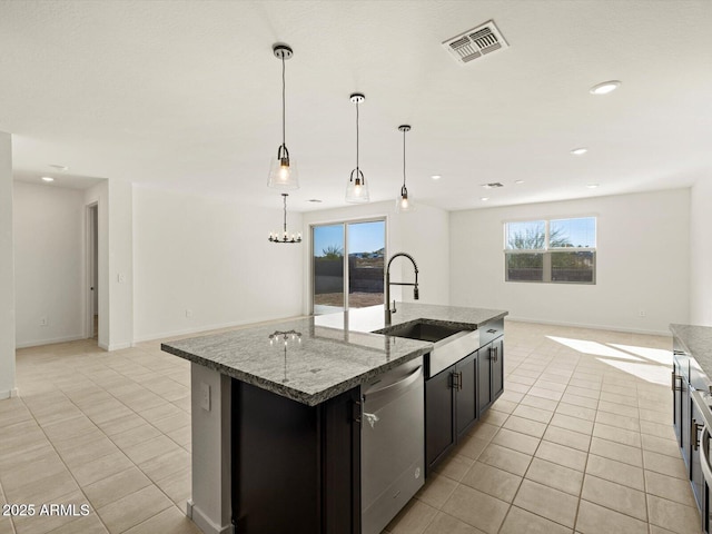 kitchen featuring sink, decorative light fixtures, stainless steel dishwasher, dark stone counters, and a kitchen island with sink