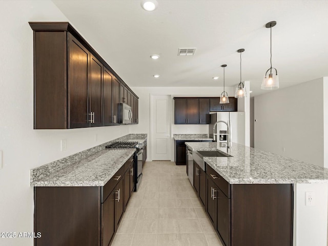 kitchen featuring pendant lighting, a kitchen island with sink, light stone counters, dark brown cabinetry, and stainless steel appliances