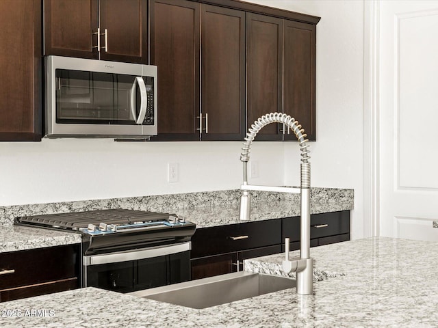 kitchen featuring dark brown cabinetry, appliances with stainless steel finishes, light stone countertops, and sink