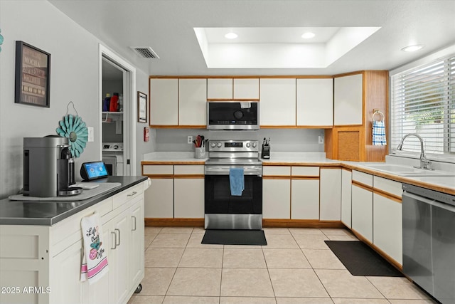 kitchen with a tray ceiling, stainless steel appliances, a sink, visible vents, and white cabinets