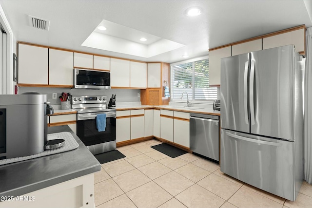 kitchen with light tile patterned flooring, visible vents, stainless steel appliances, a raised ceiling, and a sink
