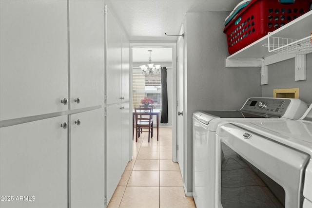 laundry room featuring washing machine and clothes dryer, cabinet space, an inviting chandelier, and light tile patterned floors