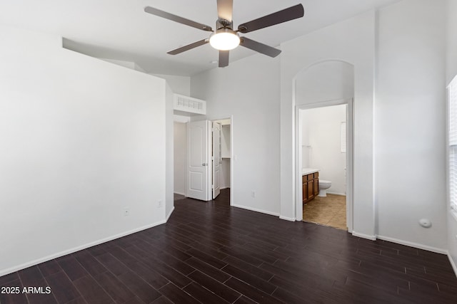 unfurnished bedroom with ceiling fan, ensuite bath, dark hardwood / wood-style flooring, and a high ceiling