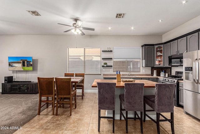 kitchen with a center island, stainless steel appliances, light tile patterned floors, wooden counters, and ceiling fan