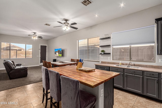 kitchen with ceiling fan, light tile patterned floors, wooden counters, and a center island