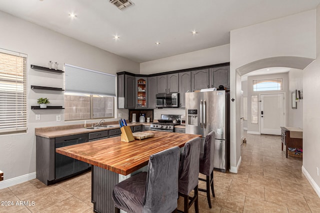 kitchen featuring sink, a center island, stainless steel appliances, a breakfast bar, and wood counters