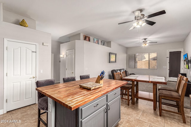 kitchen with a kitchen breakfast bar, a kitchen island, gray cabinets, ceiling fan, and wood counters