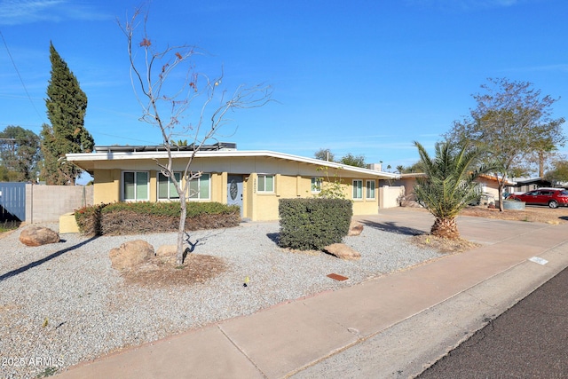 view of front facade with stucco siding, roof mounted solar panels, and fence