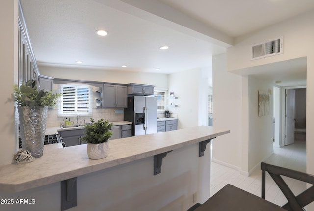 kitchen with visible vents, gray cabinets, stainless steel refrigerator with ice dispenser, tasteful backsplash, and a peninsula