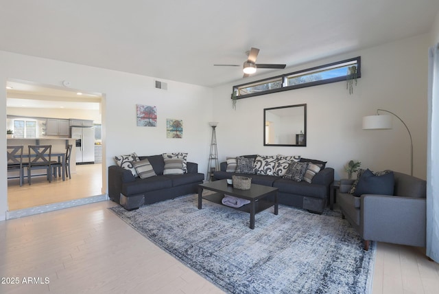 living room featuring light wood-style flooring, a ceiling fan, and visible vents