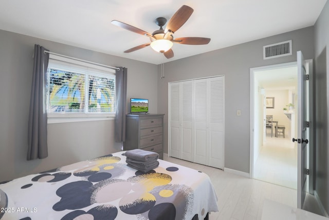 bedroom featuring light wood-type flooring, visible vents, a closet, baseboards, and ceiling fan