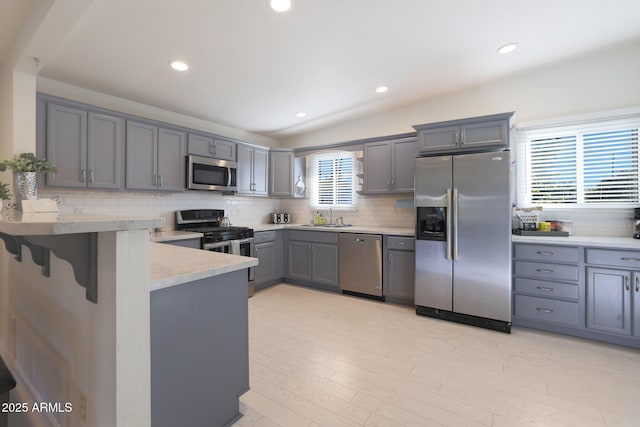 kitchen with a peninsula, gray cabinets, a sink, stainless steel appliances, and light countertops