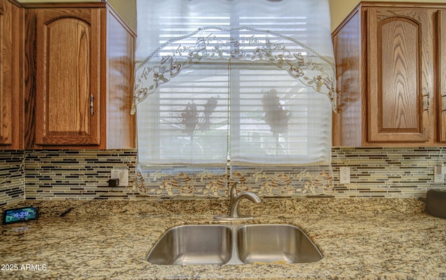 17374 W Adams St, Goodyear, AZ 85338 - kitchen with backsplash, brown cabinetry, a sink, and light stone countertops