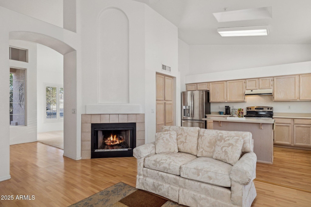 living room with light wood-type flooring, a fireplace, and high vaulted ceiling