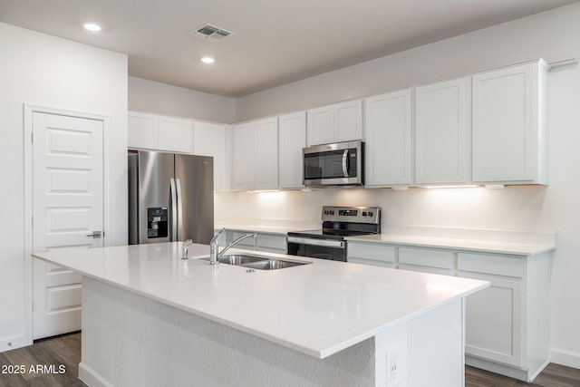 kitchen with stainless steel appliances, an island with sink, sink, and white cabinetry