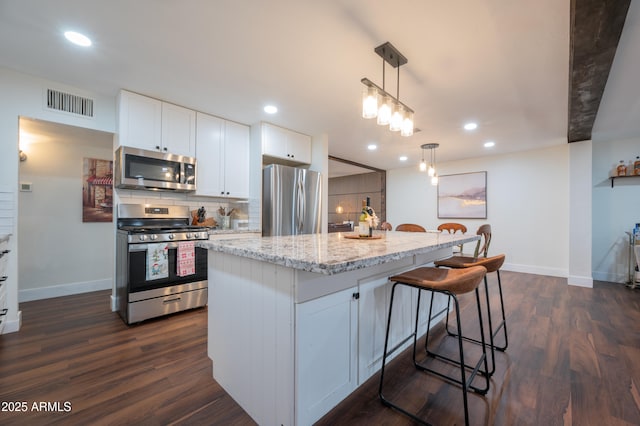 kitchen with pendant lighting, white cabinetry, stainless steel appliances, and an island with sink