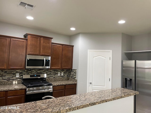 kitchen featuring decorative backsplash, appliances with stainless steel finishes, dark brown cabinets, and dark stone counters