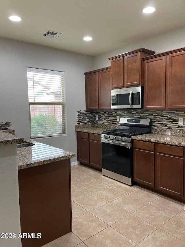 kitchen featuring tasteful backsplash, dark stone counters, dark brown cabinets, stainless steel appliances, and light tile patterned floors