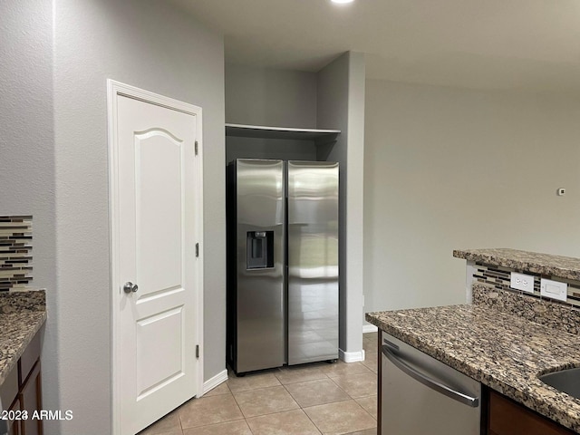 kitchen featuring decorative backsplash, light tile patterned floors, dark stone counters, and appliances with stainless steel finishes