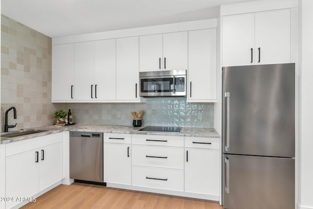 kitchen with light hardwood / wood-style floors, sink, backsplash, appliances with stainless steel finishes, and white cabinetry