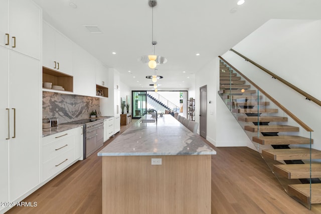 kitchen featuring sink, wood-type flooring, decorative light fixtures, a kitchen island with sink, and light stone countertops