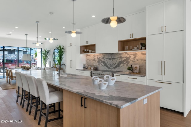 kitchen with light stone counters, an island with sink, sink, and white cabinetry