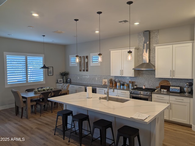 kitchen with stainless steel stove, decorative light fixtures, sink, white cabinets, and wall chimney range hood