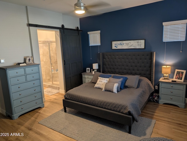 bedroom featuring a barn door, ceiling fan, connected bathroom, and light hardwood / wood-style floors