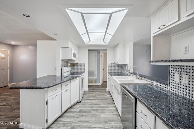 kitchen featuring white appliances, light wood-type flooring, a sink, a peninsula, and white cabinets