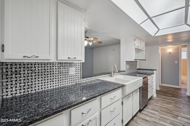 kitchen with tasteful backsplash, white cabinetry, light wood-style floors, stainless steel dishwasher, and ceiling fan