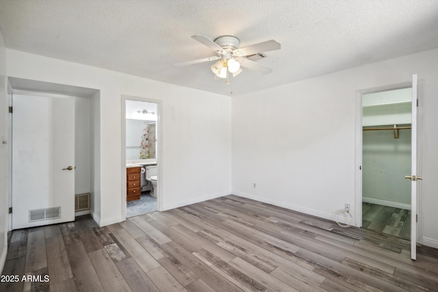 unfurnished bedroom with wood finished floors, a textured ceiling, baseboards, a ceiling fan, and connected bathroom