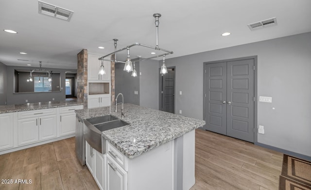 kitchen with sink, hanging light fixtures, light stone counters, white cabinets, and a center island with sink