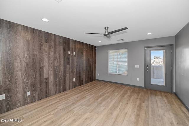 unfurnished room featuring ceiling fan, light hardwood / wood-style floors, and wood walls