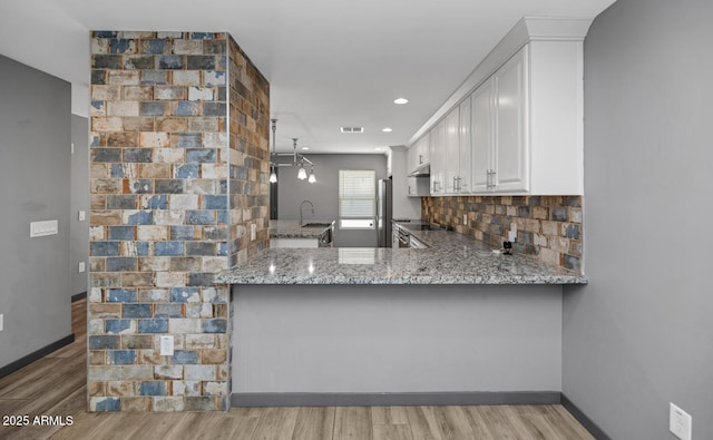 kitchen with sink, backsplash, light stone counters, white cabinets, and kitchen peninsula