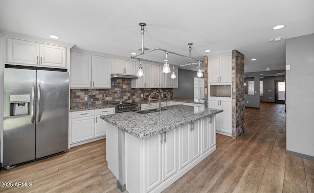 kitchen with sink, white cabinetry, hanging light fixtures, appliances with stainless steel finishes, and a kitchen island with sink